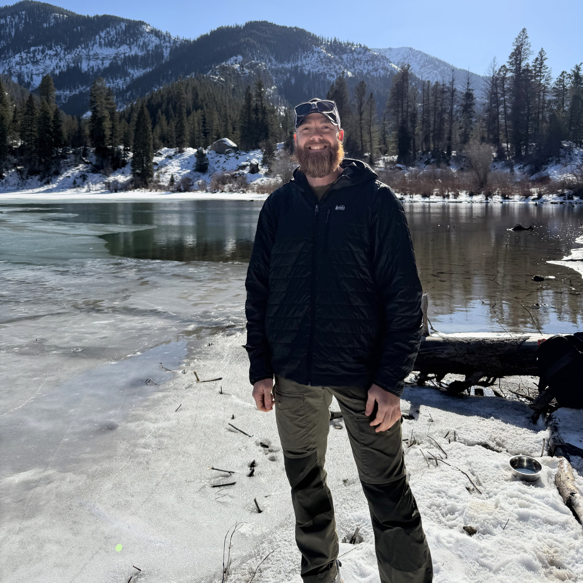 Nick Mann outdoors with mountains and a lake behind him